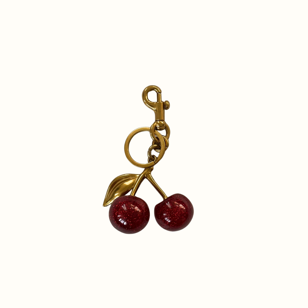 Gold cherry keychain or bag charm with red stones on a white background
